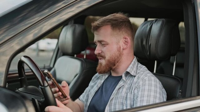 Happy young man looking at phone screen while sitting in the car. Slow motion