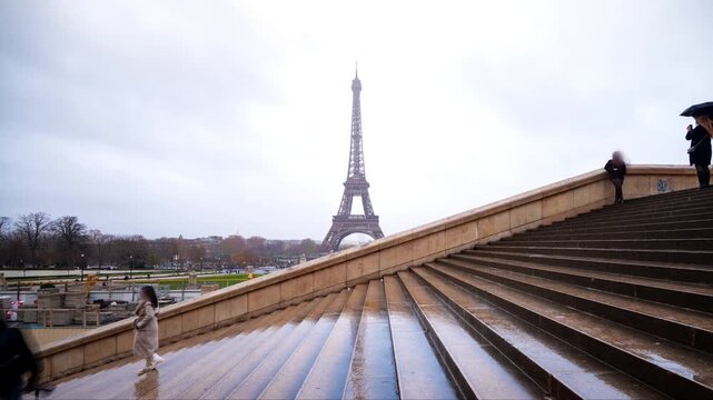 Eiffel tower timelapse in Paris with with motion blurred people walking on wet Trocadero stone steps under an overcast sky