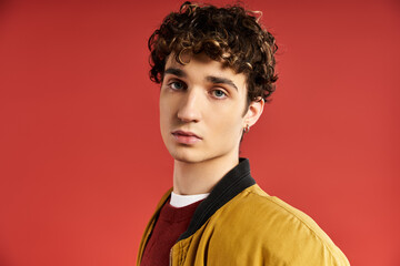 Obraz premium Charming young man in stylish jacket poses against vibrant red backdrop showcasing modern fashion