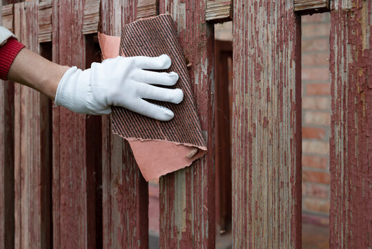 Person restoring a wooden fence with a sanding block in the late afternoon