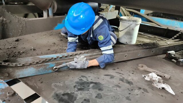 Maintenance worker removing old rubber cleaner from industrial belt conveyor.