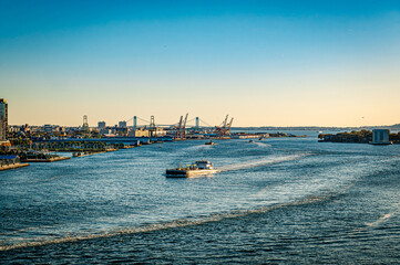 Fototapeta premium Industrial ship moving through water with port cranes and bridge in the background.