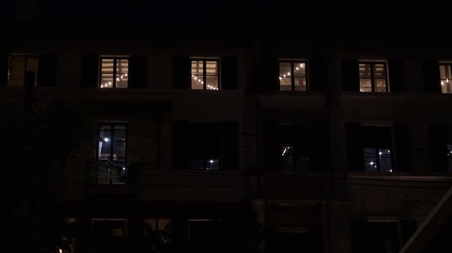 A quiet and serene night scene with a row of houses lit up. The houses are situated close together, creating a sense of community and warmth. The lights on the houses are dim
