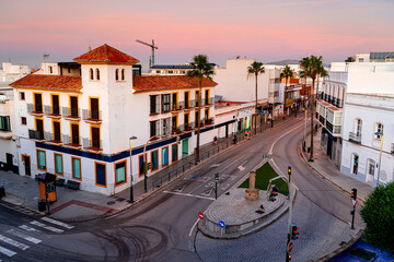 Obraz premium Crossing a street without people with palm trees and traditional houses at sunrise, Spain, Tarifa.
