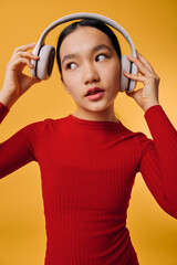 Young woman in red sweater adjusting wireless headphones, listening music with thoughtful expression on orange background. Technology, lifestyle and fashion with casual outfit and gadget.