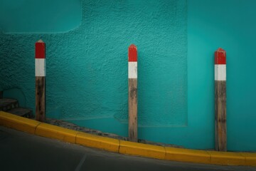 Three Wooden Posts with Red and White Tops Against Turquoise Wall yellow curb road