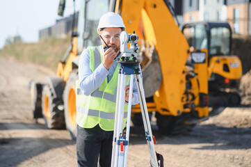 Surveyor communicating while operating a theodolite at construction site