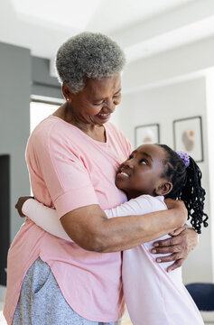 African American senior woman and child hugging, wearing pastel pink tops with framed art at home