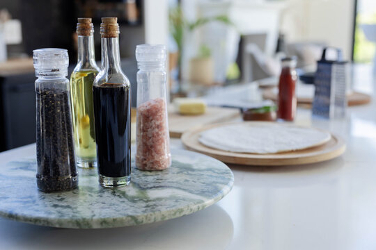 Four condiments sitting on marble turntable on glossy counter, tortillas blurred behind