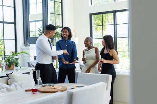 Four adults are standing in bright modern living area by dining table with wooden serving board