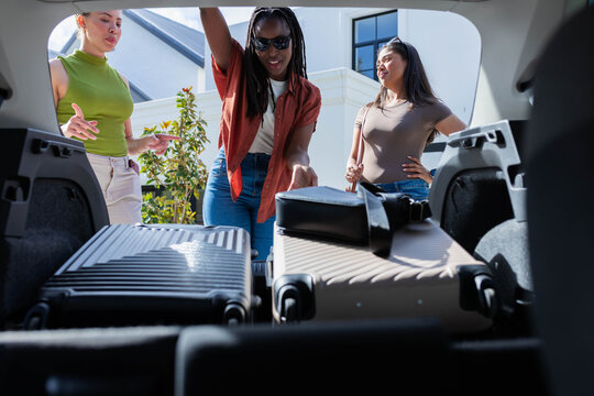 African American women loading hard-shell suitcases into open SUV trunk on sunny driveway