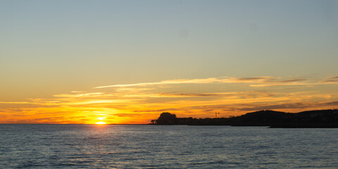 A serene sunset over a calm body of water with a distant landscape © Rodrigo