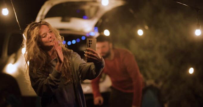 Couple shares moments together in car at night with string lights and a friend nearby