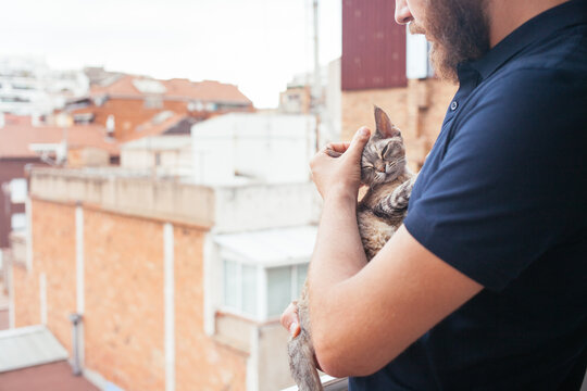 Man gently holding sleeping cat on balcony, tender pet owner bonding moment in city apartment