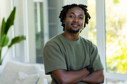 Adult male standing arms crossed in living room near windows, wearing olive shirt and watch