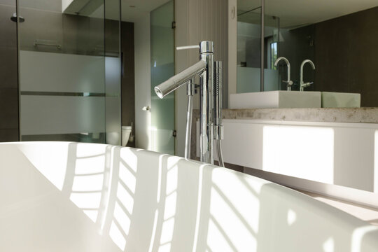 White tub is soaking in bathroom window light with blinds casting shadows, chrome faucet nearby