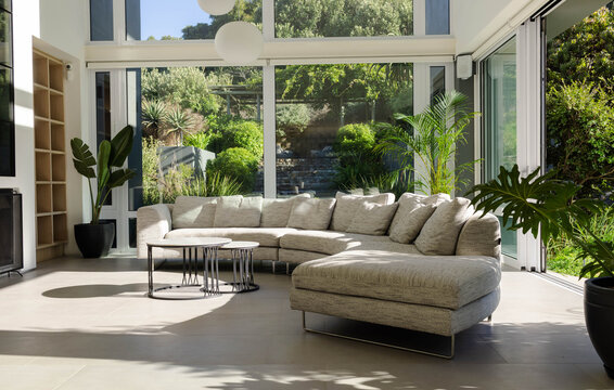 Curved light-gray sectional with chaise is sitting in living room near glass doors, coffee tables