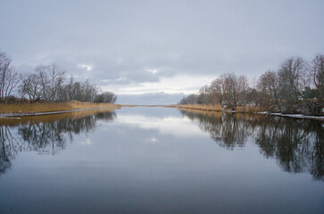 J&auml;gala river close to it`s mouth in the gulf of Finland, with bare trees m reed and clouds reflecting in the water 