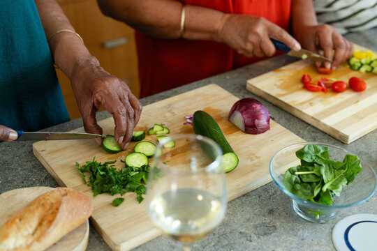 Vegetables are being sliced on gray stone countertop with cutting boards, crusty bread, wine glass
