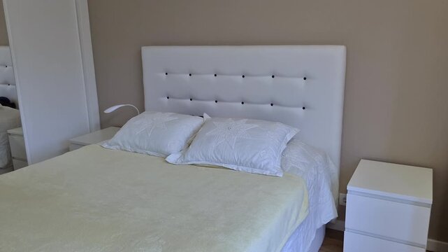 Neatly made double bed with padded white headboard, soft bedding and bedside tables in a bright home bedroom, illustrating clean domestic interior, comfort and everyday organization.