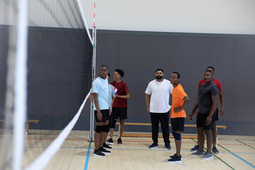 Fototapeta premium Diverse six men standing on gym volleyball court by net antenna, holding volleyball, with knee pads