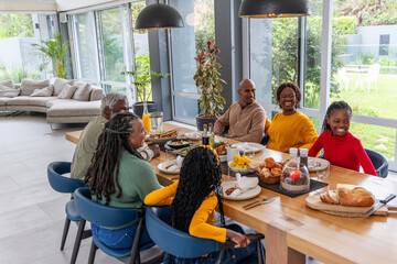 African American family with seniors and children sitting at table sharing meal passing bread