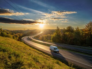 White delivery van driving on a winding highway through an autumn landscape at sunset © am