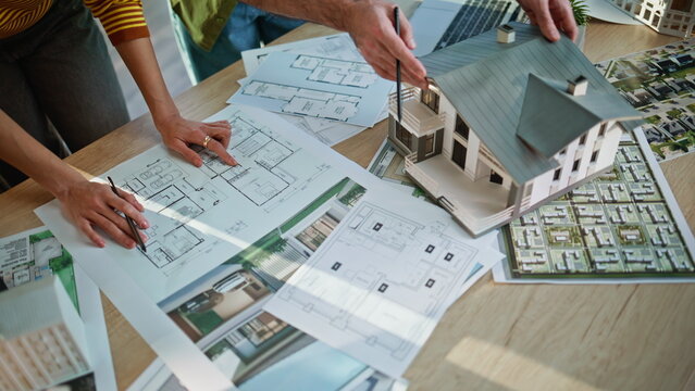 Architects hands pointing blueprints analyzing building model at office closeup.