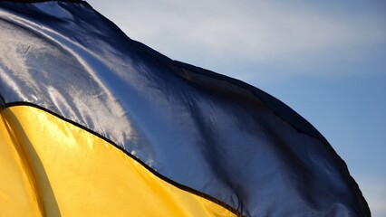 Blue-yellow symbol of Ukraine waving at wind against the background of sunlight. Ukrainian flag illuminated by sun fluttering at countryside. Concept of peace and support against russian aggression
