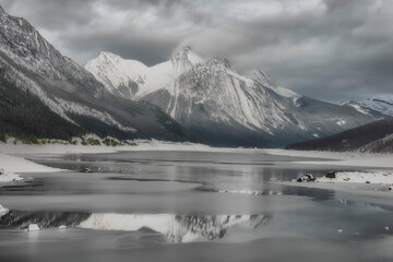 Professional landscape of snow-capped peaks reflecting in a frozen mountain lake. Moody overcast...