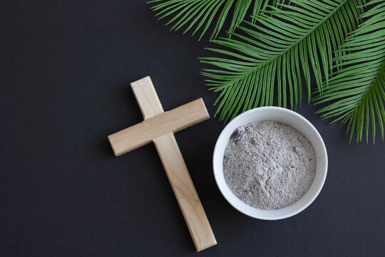 Wood cross, bowl of ashes and palm branches on black