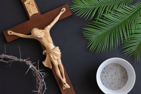 Crucifix with bowl of ashes, palm leaves and crown of thorns on black background