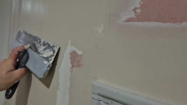 Slow motion close-up of a worker's hand smoothing putty on a drywall joint with a trowel.