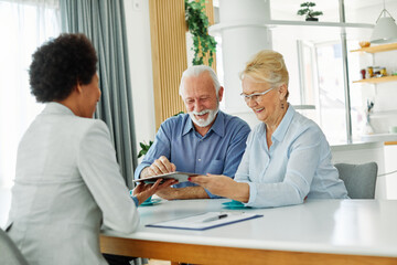 Obraz premium Senior couple having a meeting with an agent using a tablet computer , businesswoman, salesperson or doctor in his office