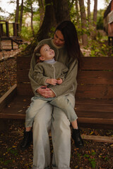 The daughter sits on her mother's lap and looks into her mother's eyes. A family is swinging on a wooden swing in the park. The interaction of a mother and a girl. Vertical photo. Mothers Day. 
