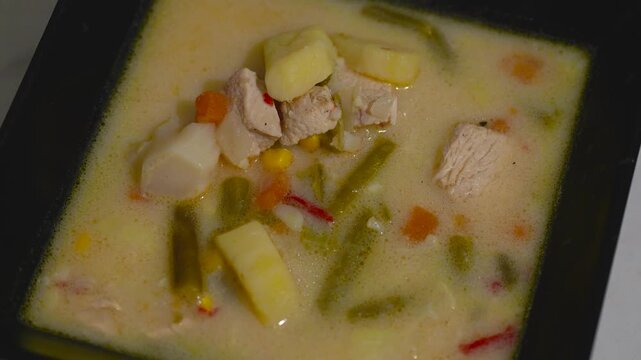 Freshly cooked hot meat soup in a black square bowl with rising steam
