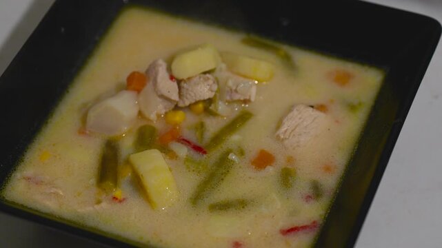 Freshly cooked hot meat soup in a black square bowl with rising steam
