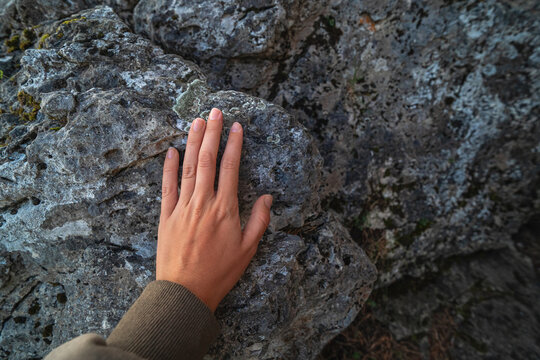 A woman touches the rocks with her hand to feel an energetic connection with nature
