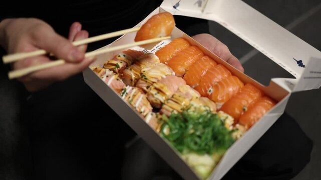 close up shot of chopsticks carefully picking up a fresh sushi roll from a takeaway box food delivery concept modern urban lifestyle enjoying asian cuisine at home detailed texture of rice salmon