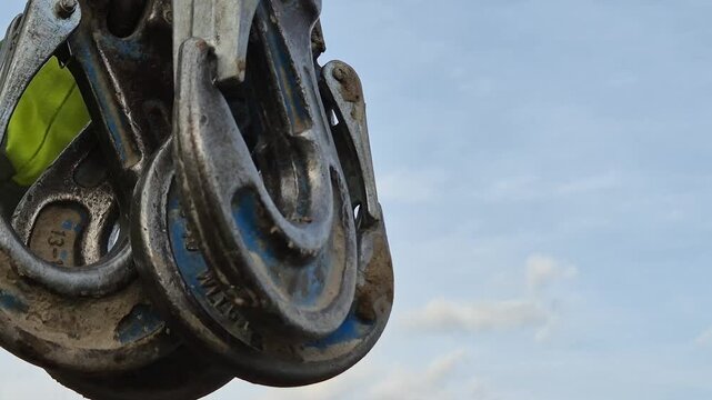Close-up of a construction worker's hands gathering four crane chain slings and hooks.