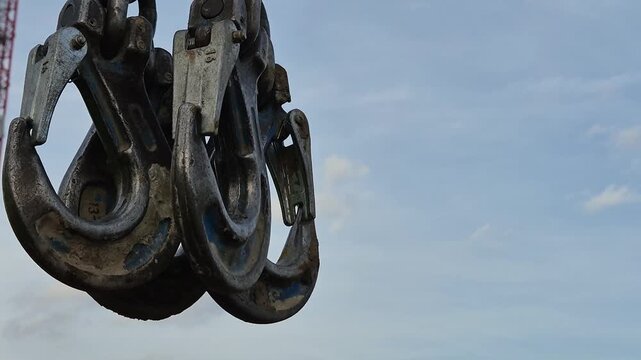 Slow motion close-up of a construction worker's hands gathering four heavy steel crane hooks and chain slings.