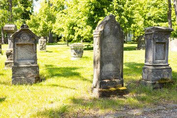 Fototapeta premium Weathered gravestones in a old peaceful cemetery surrounded by lush green trees and grass, showcasing intricate carvings and historical significance in a serene setting