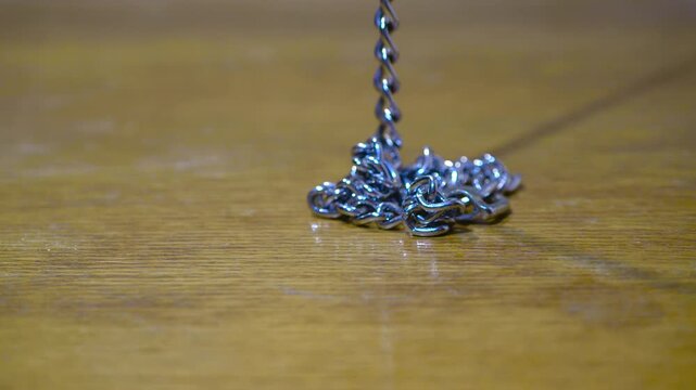 Heavy metal chain falling onto wooden table surface with metallic clink sound