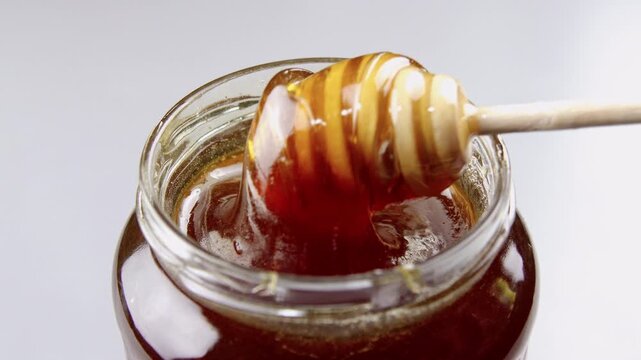 Close Up Golden Honey Dipper In Jar, Sunlit Kitchen Setting With Viscous Amber Honey Wrapping Wooden Grooves,