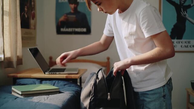 White teenage boy packing books into backpack for school in bedroom interior - education responsibility and daily routine during adolescence concept