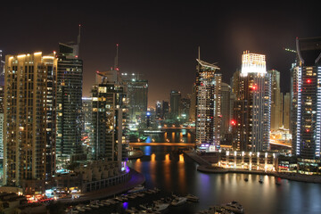 Obraz premium Stunning night view of Dubai Marina skyline featuring illuminated skyscrapers, luxury yachts, and golden reflections on the dark canal water.