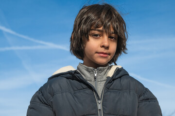 Young boy standing outdoors under blue sky during winter