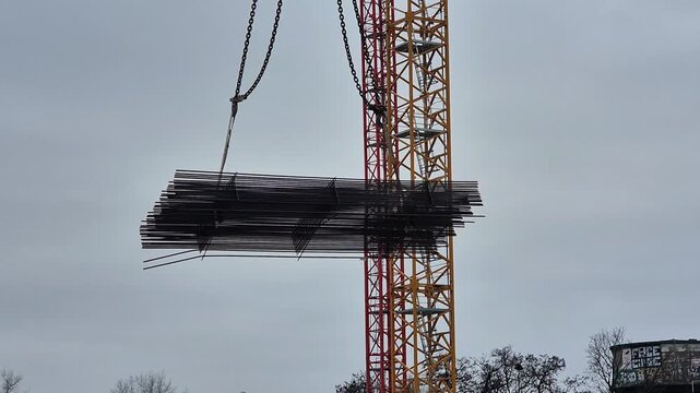 Slow motion shot of a crane lowering a steel rebar bundle, finishing with a construction worker's hand reaching out to guide it.