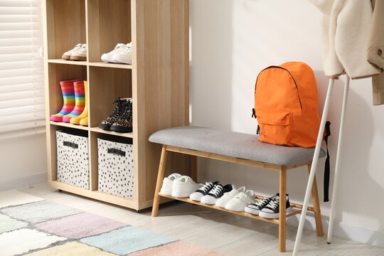 Different stylish children's shoes on shelves, backpack and hanger with coat in entryway