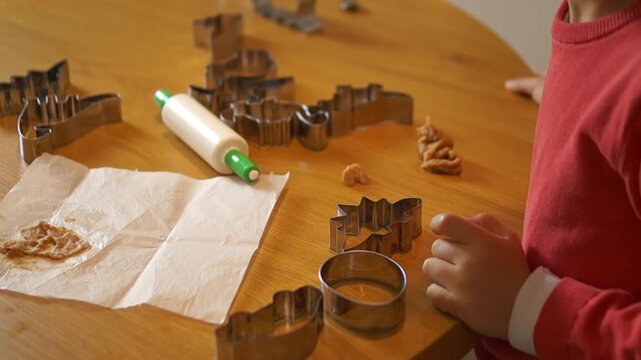 A playful and hungry young child leans down to bite into raw cookie dough sitting on a wooden table, skipping the use of hands for a funny and spontaneous moment during a home baking activity.